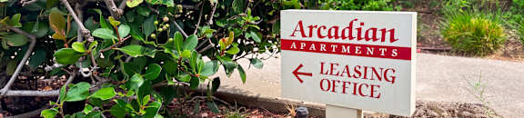 A sign for Arcadian Apartments leasing office is in front of a bush.