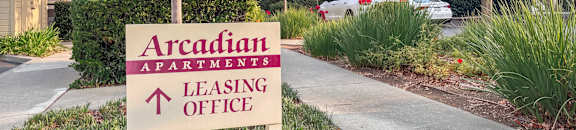 A sign for Arcadian Apartments leasing office stands in front of a building.