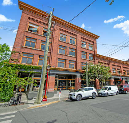 A street view of a red brick building with cars parked in front.