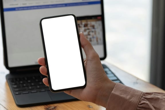 a person holding a smartphone in front of a laptop computer