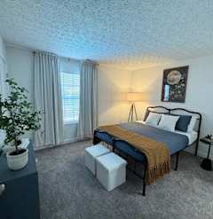 A bedroom with a bed, nightstand, and a potted plant.
