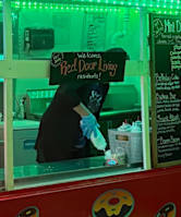 A person in a black shirt and blue gloves is behind a counter with a sign that says "Welcome Red Door Living residents!".