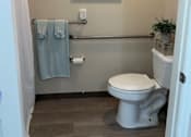 Thumbnail 2 of 9 - A bathroom with a toilet, a towel, and a painting on the wall.