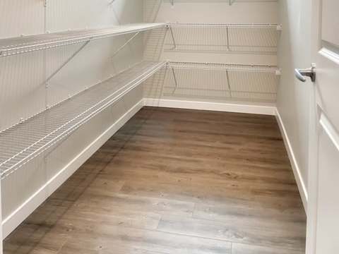 Empty walk-in closet with wooden floors and white shelves.