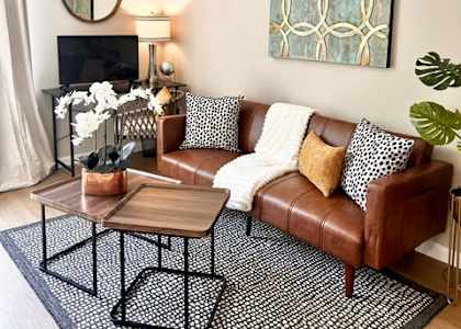 A living room with a brown leather couch, a coffee table, and a painting on the wall.