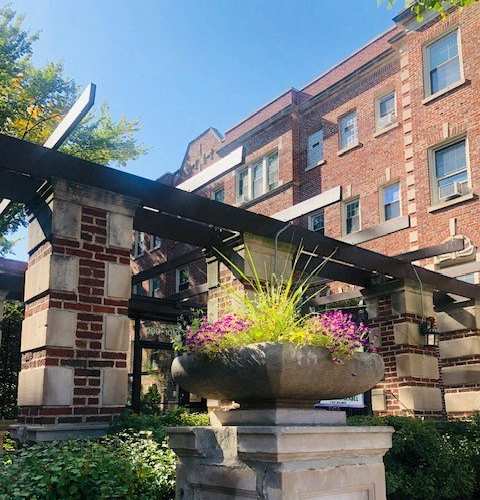 A large stone planter with purple flowers sits in front of a brick building.