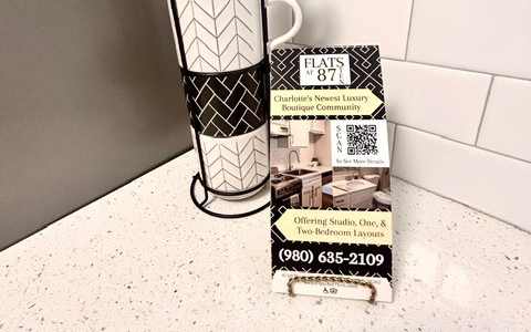 A black and white patterned mug sits next to a business card for a real estate agency.