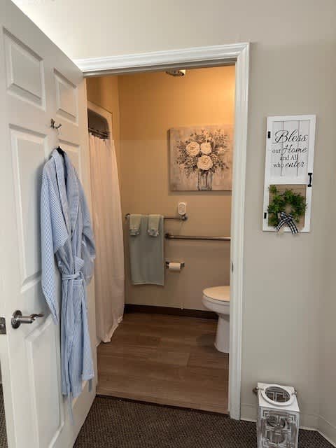A bathroom with a toilet, a shower curtain, a towel, and a robe hanging on the door.