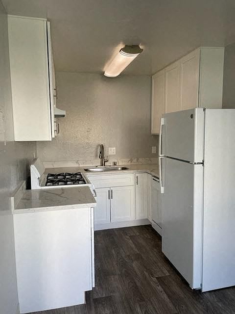 A white kitchen with a refrigerator, sink, and stove.