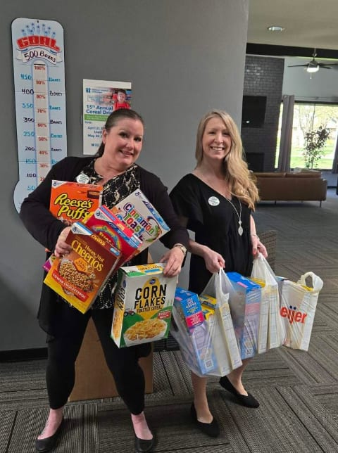 Two women holding bags of groceries in front of a sign.
