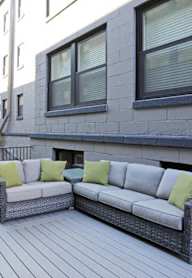 A patio with a grey wicker couch and green pillows.
