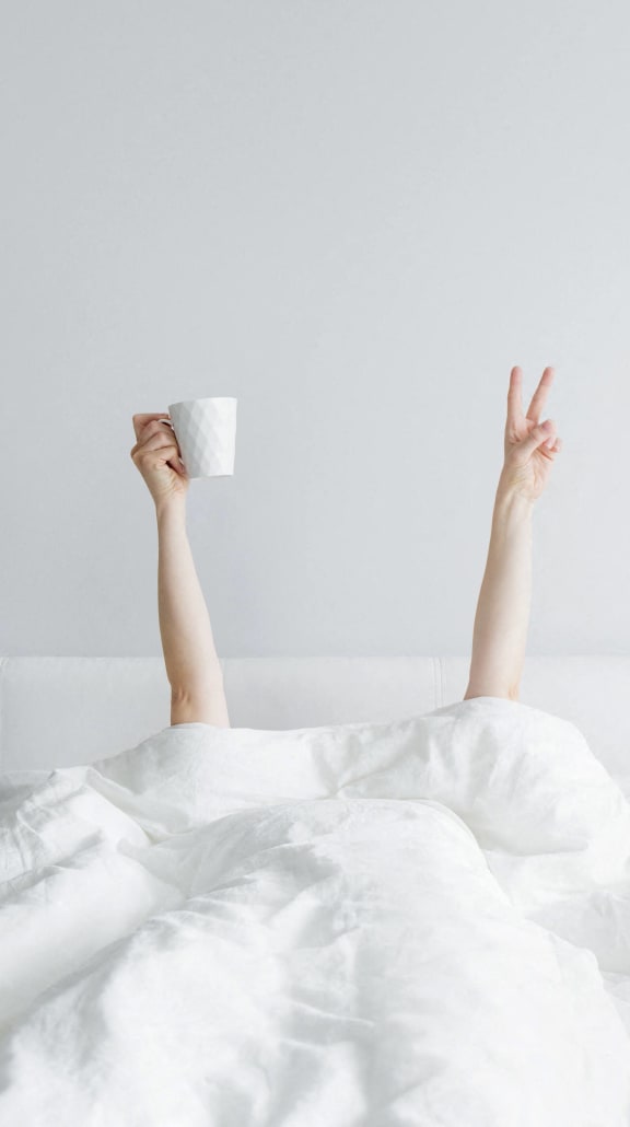 a woman waking up in bed with a cup of coffee