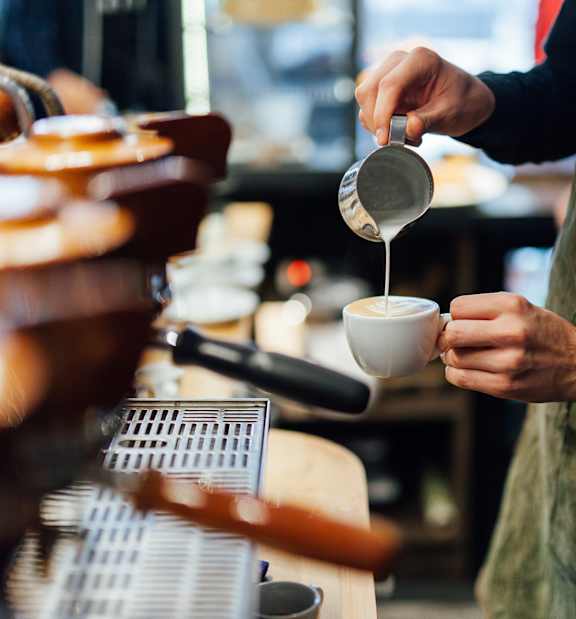 A person in an apron is pouring a liquid from a container into a cup.