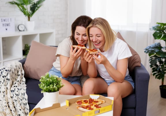 two girls sitting on a couch and eating pizza