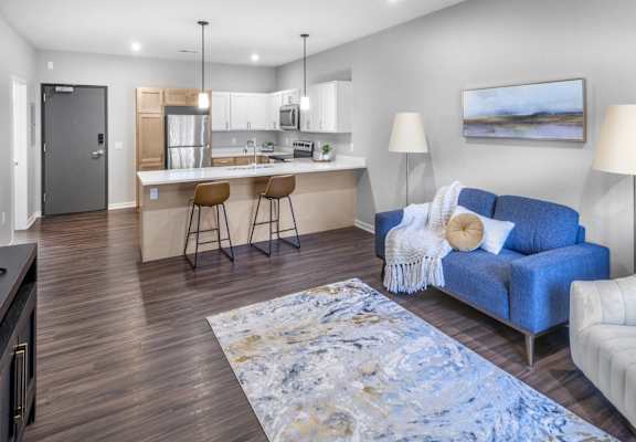 A modern living room with a blue couch and a kitchen area in the background.