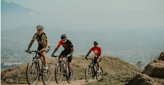 three men riding bikes on a hill with a city in the background