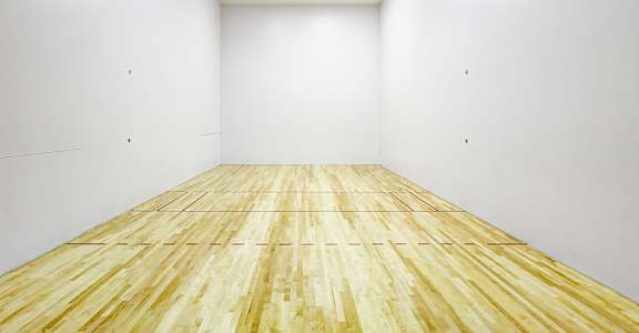 A squash court with wooden flooring and white walls.