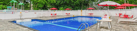 a swimming pool with chairs and umbrellas and a blue pool at Station Pointe, Mansfield, 02048