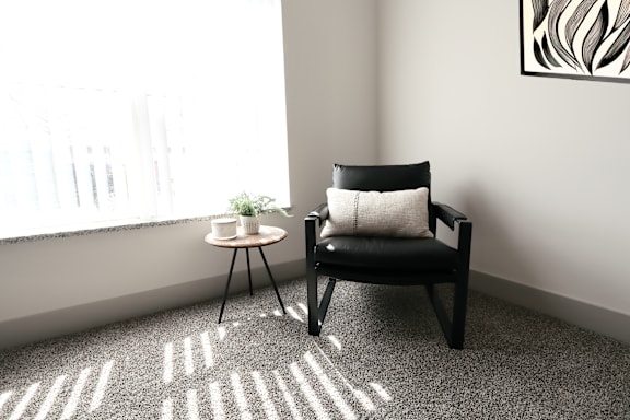 A black chair with a white pillow sits in front of a window with a small table beside it.