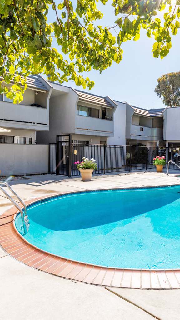 A swimming pool in a backyard with a white fence and a house in the background.