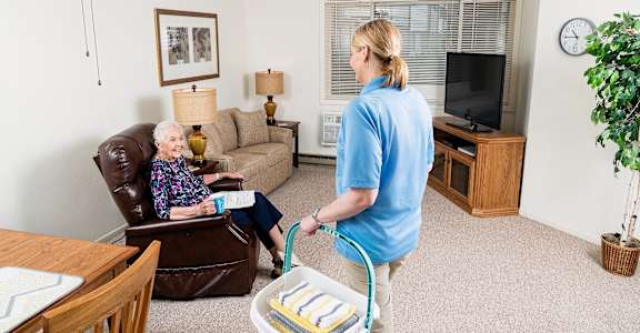 a woman vacuuming a living room with an older woman in a chair
