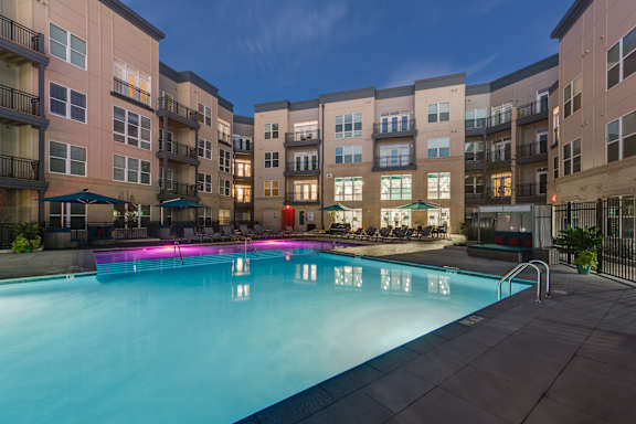 A swimming pool in front of apartment buildings at dusk.