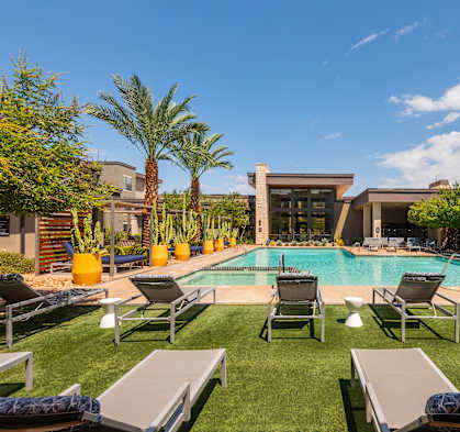 A pool surrounded by lounge chairs and palm trees.