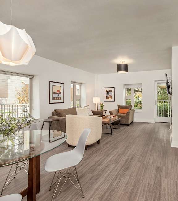 A modern living room with a glass dining table and white chairs.