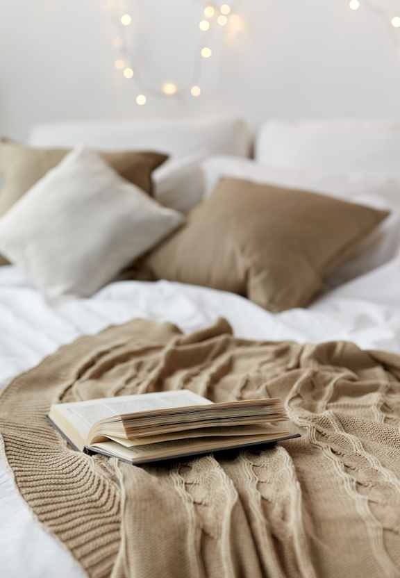A bed with a white comforter and a brown blanket with a book on it.at The Residences at Southern Oaks, Petersburg, 23805
