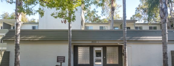 the entrance to a white building with a sidewalk and trees