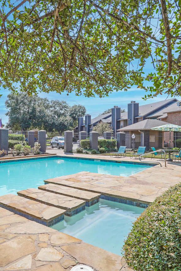 A swimming pool surrounded by a stone patio and green bushes.