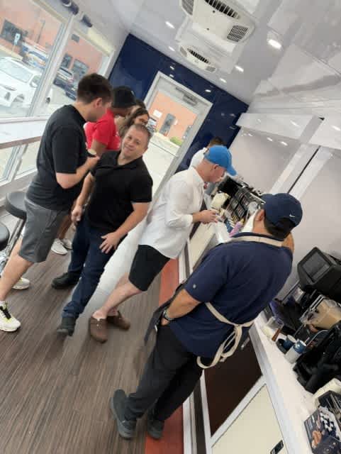 A group of people are gathered around a counter in a room with a ceiling fan.