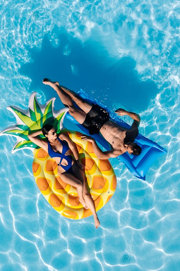 A person is floating on a pineapple in a pool.
