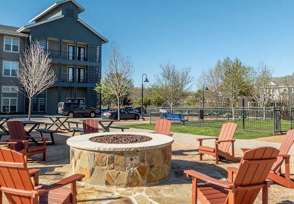 an outdoor fire pit with rocking chairs in front of an apartment building