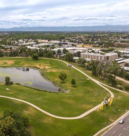 an aerial view of a park with a pond and a city in the background