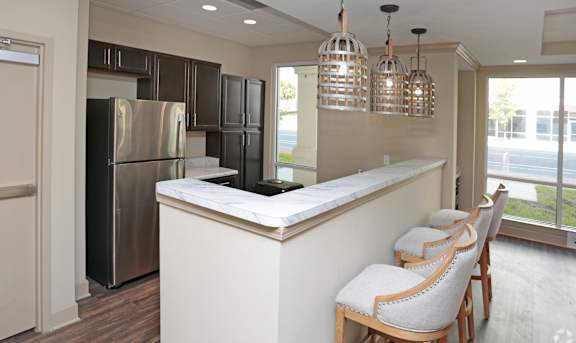 A kitchen with a refrigerator, bar stools, and pendant lights at Arbours at Tumblin Creek ~ Active 55+ Adult Community, Gainesville 32608