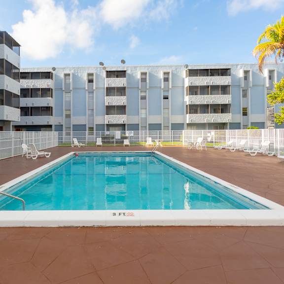 A large outdoor pool surrounded by a fence and chairs.