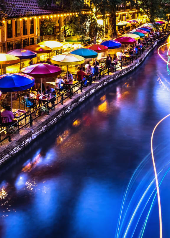 a city at night with lights on the river and umbrellas
