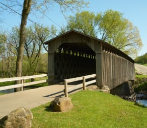 a covered bridge is next to a road and a river at The Daniels at Northern Gateway, Wisconsin