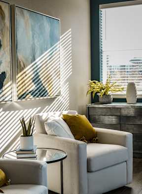 A white couch with a yellow pillow is in front of a window with blinds.