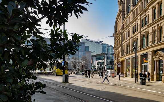 A city street with people walking and a tram on the tracks.