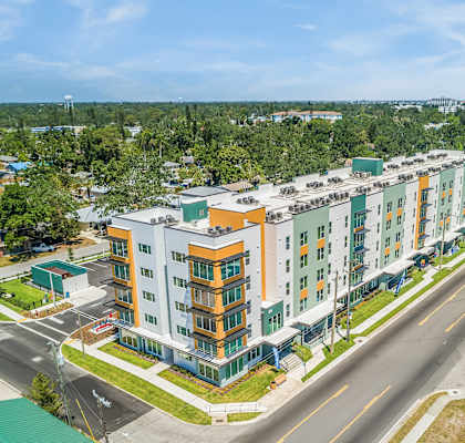 A multi-story apartment building with a green roof is surrounded by a road and other buildings.