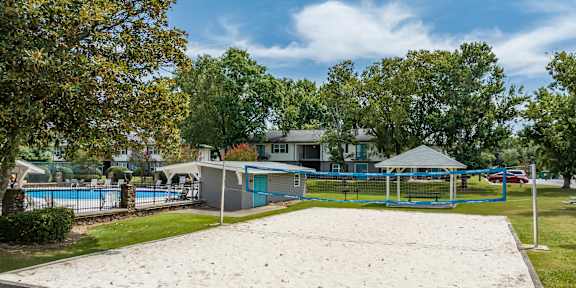 A sand volleyball court in a park with trees and a building in the background.