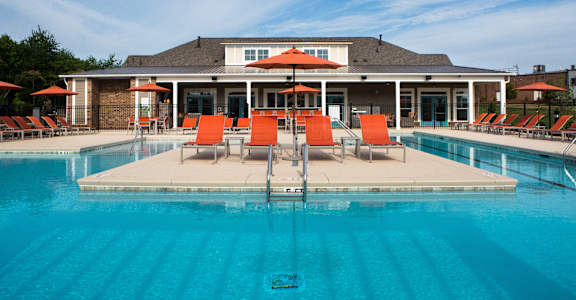 a swimming pool with orange chairs and umbrellas in front of a house