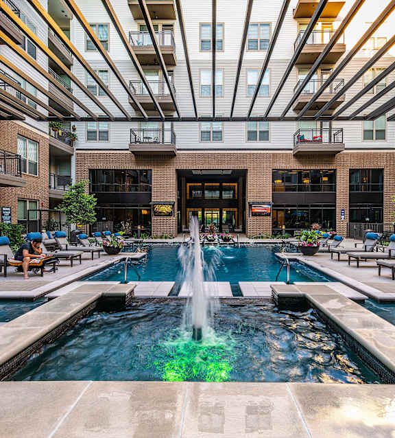 A large fountain in the middle of a pool surrounded by lounge chairs.