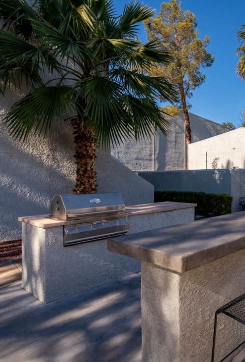 a patio with a grill and chairs next to a pool