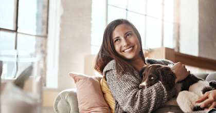 A woman is sitting on a couch holding a dog.