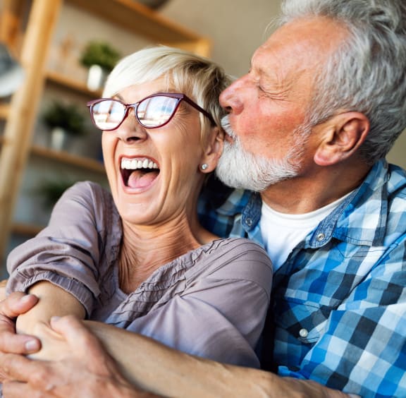 an older couple laughing together while sitting on a couch