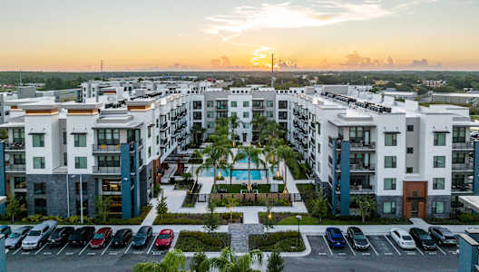 an aerial view of an apartment complex with a parking lot and palm trees at 19 South Apartments in Kissimmee, FL