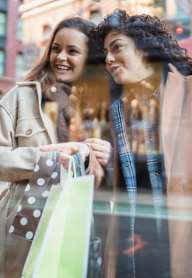Two women are standing outside a store, one holding a shopping bag.